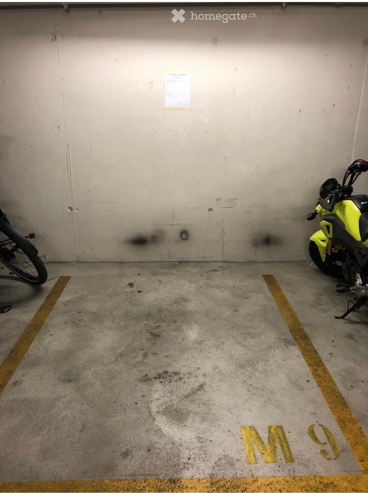 Underground parking space with concrete floor and walls, marked parking spots, and two motorcycles parked.