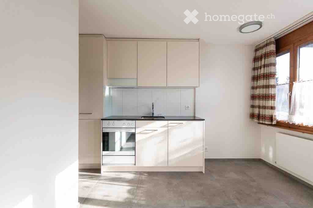 Modern kitchen with white cabinets, stainless steel oven, sink, and a window with striped curtains.