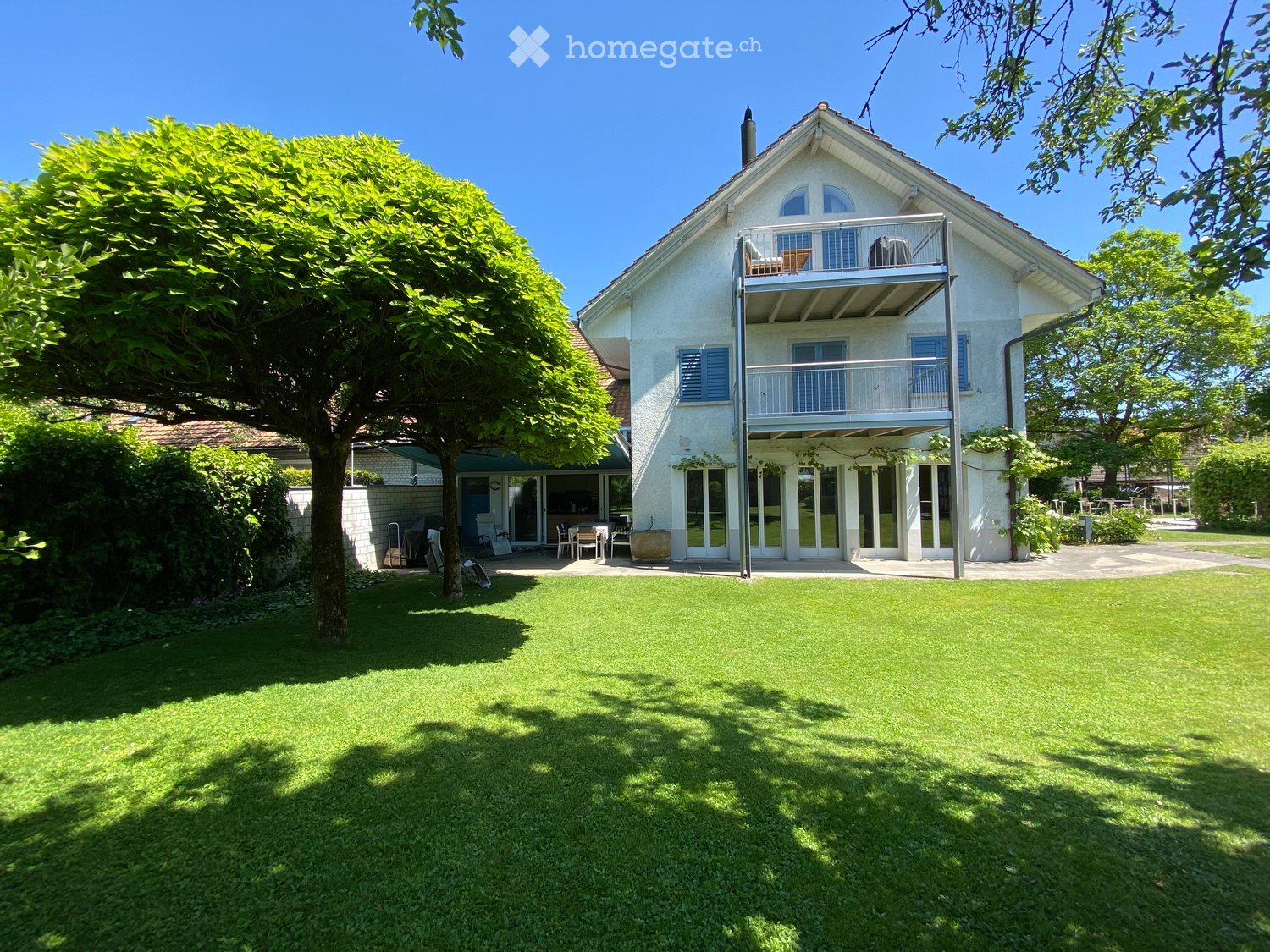 Two-story house with white exterior, blue shutters, balcony, and well-maintained lawn.
