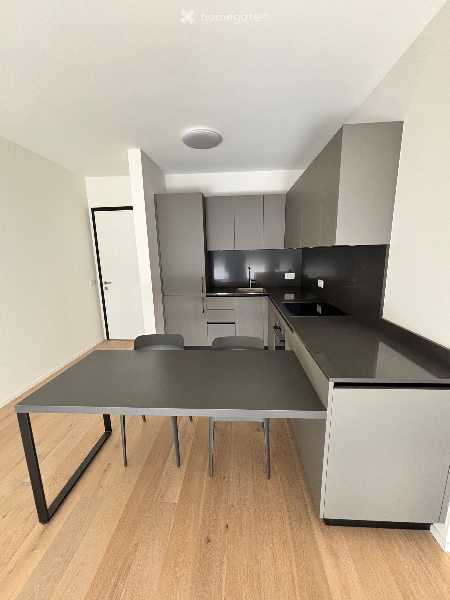 Modern kitchen with grey cabinets, black countertops, a dining table with chairs, and a sink area.