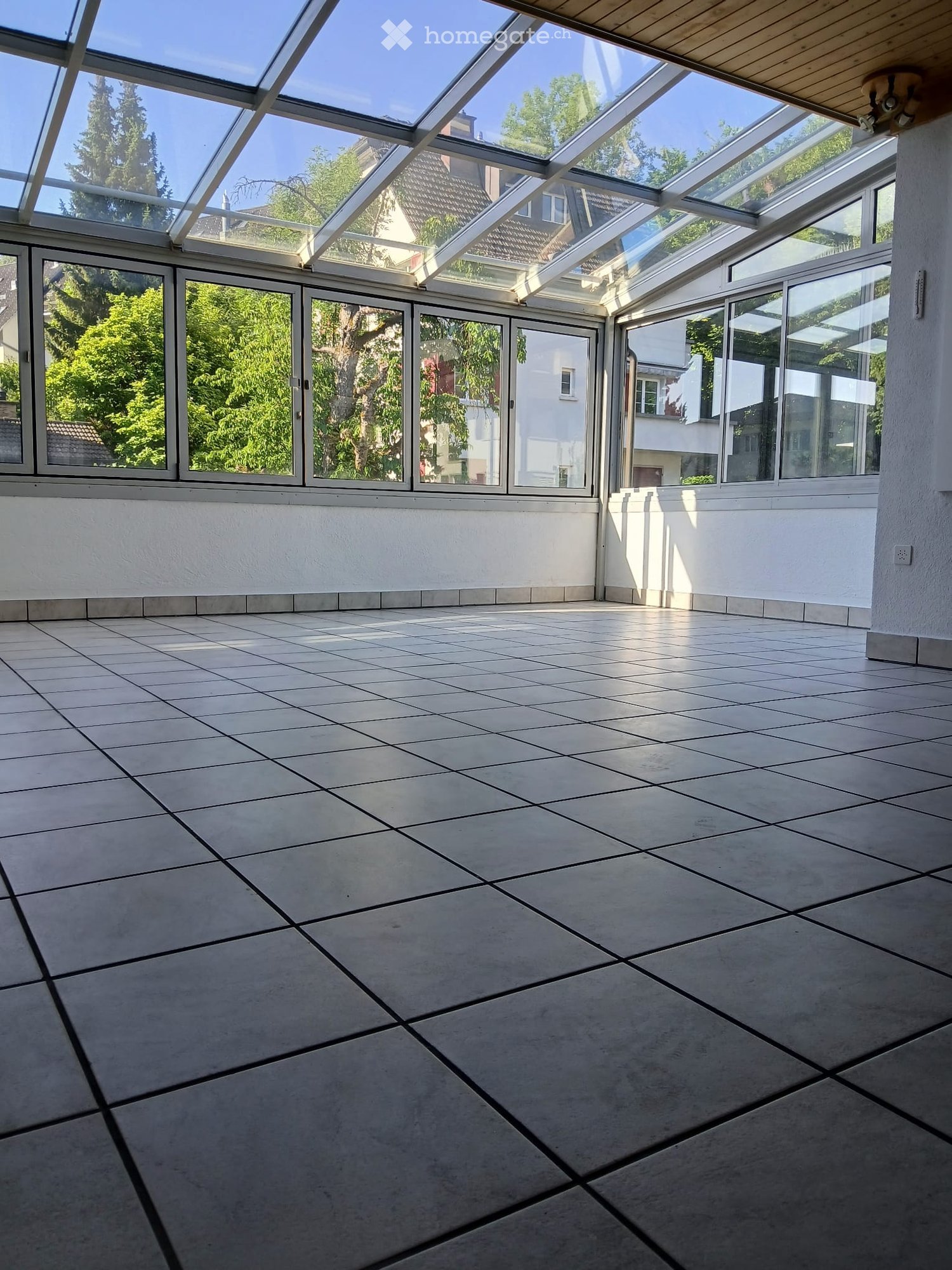 Empty room with tiled floor, large glass windows and a glass roof, allowing natural light to fill the space.