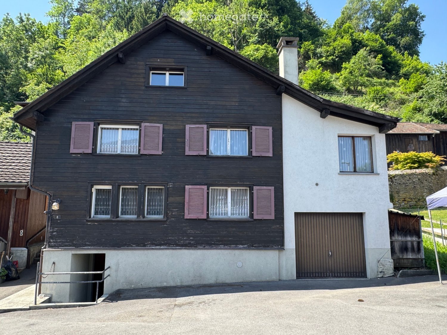 Two-story wooden house with dark brown exterior, white chimney, multiple windows with pink shutters, and a garage entrance.