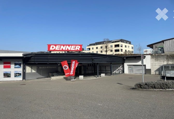 Building exterior with a large sign reading "DENNER" and a parking area.