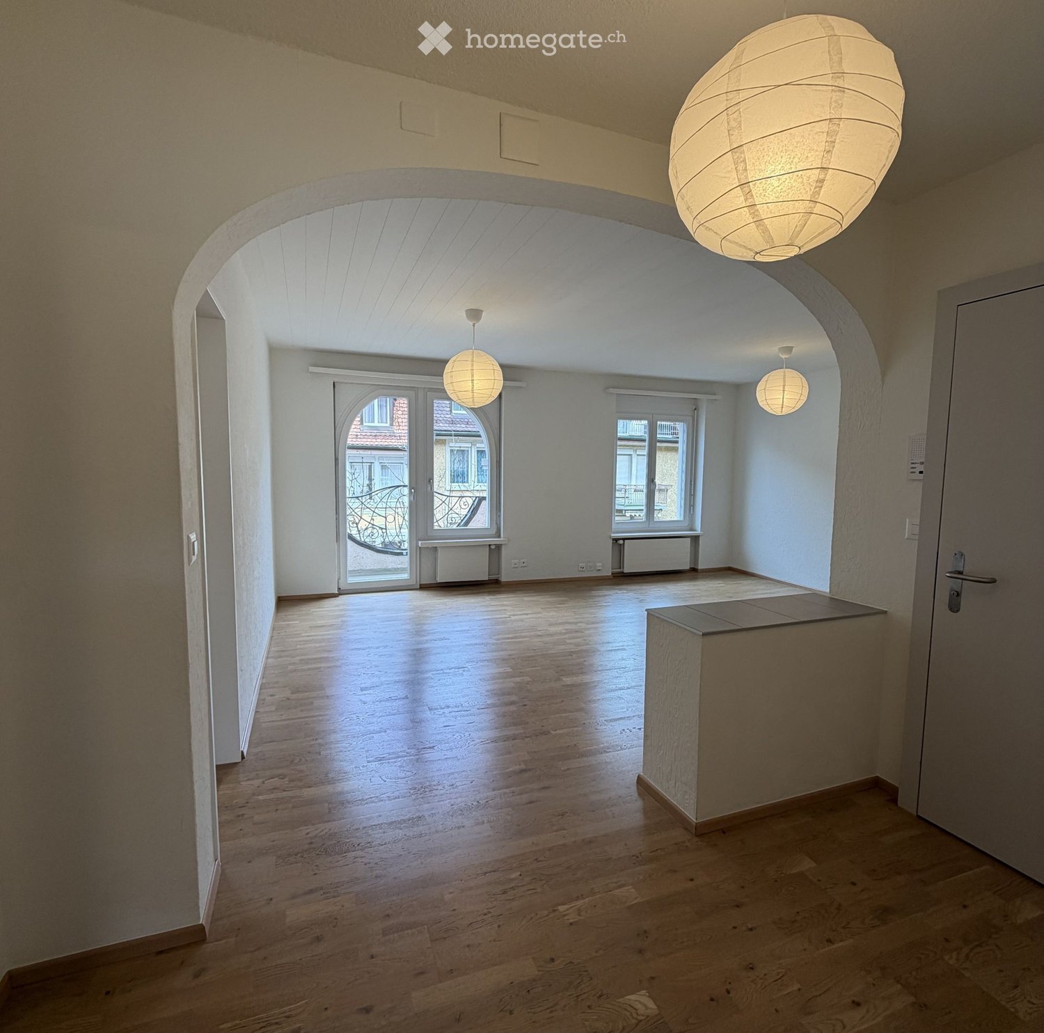 Empty room, wooden floor, white walls, arched ceiling, large windows, balcony, hanging lamps