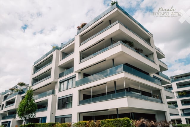 Modern multi-story residential building with balconies and greenery on the roof.