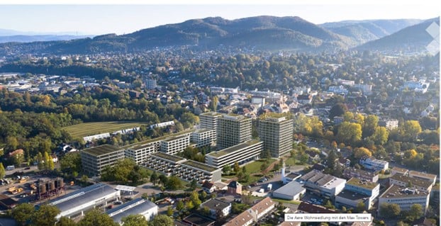 Aerial view of a modern residential complex with multiple buildings, surrounded by green spaces and trees, with a cityscape and hills in the background.