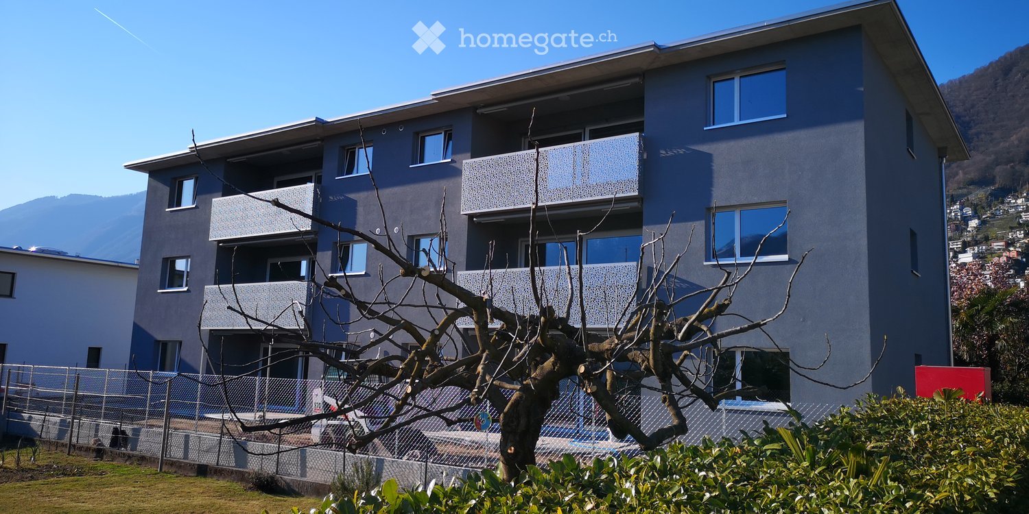 Modern multi-story apartment building with balconies, large windows, and a scenic mountain view in the background.