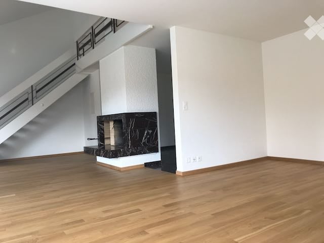 Empty room with wooden flooring, white walls, and a modern fireplace with black marble surround. A staircase is visible in the background.