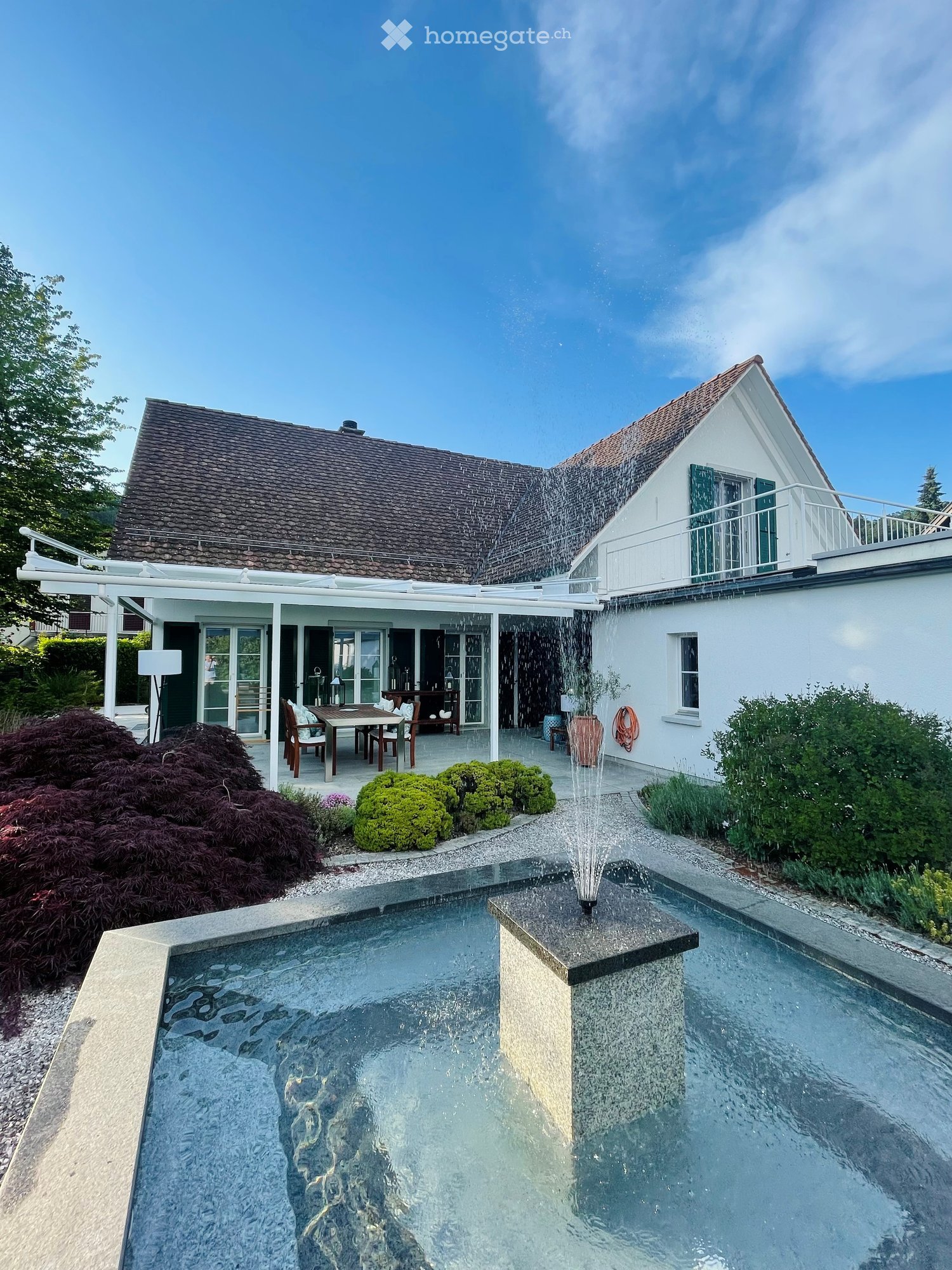 Modern outdoor area with a swimming pool, fountain, patio furniture, and well-maintained landscaping.