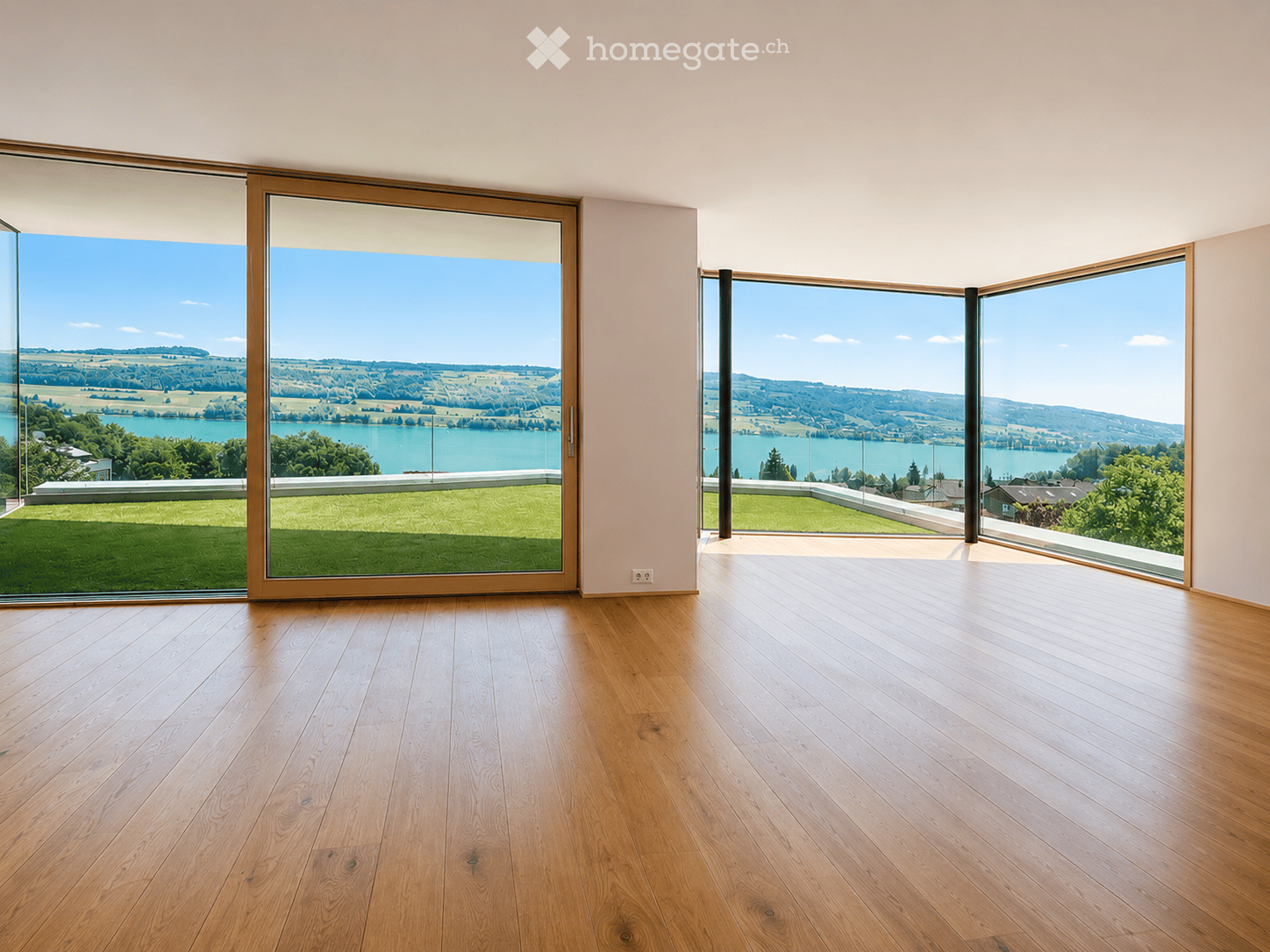 Empty room with wooden flooring, large glass sliding doors, and scenic view of a lake and landscape.