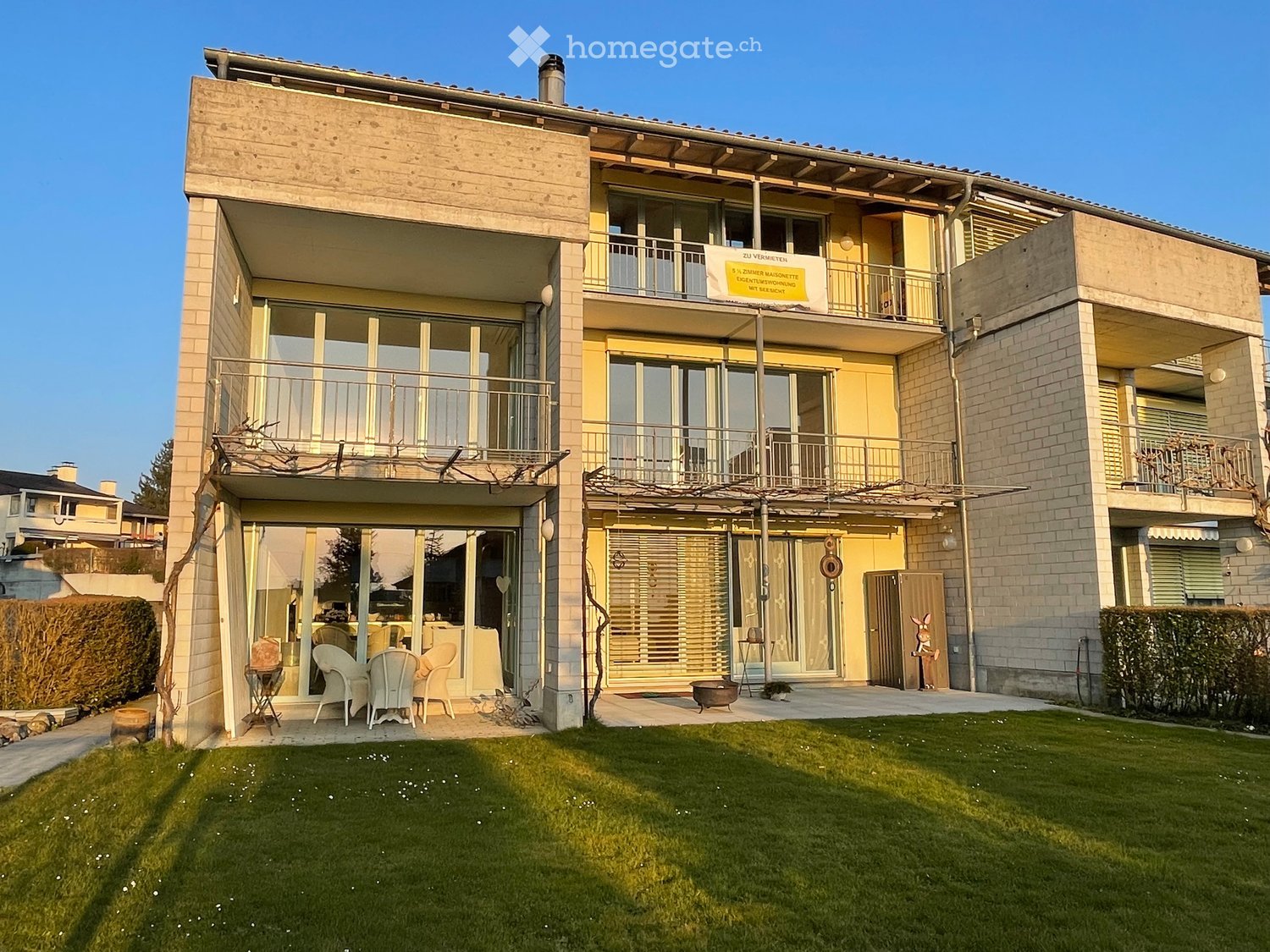 Two-story residential building with balconies, large windows, and a well-maintained lawn in front.