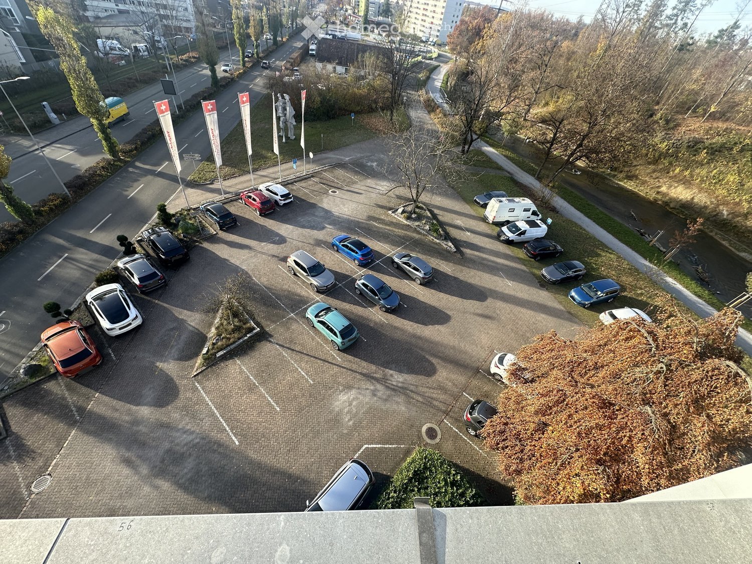 an aerial view of a parking lot with multiple cars parked, a pathway, some trees, and grassy areas