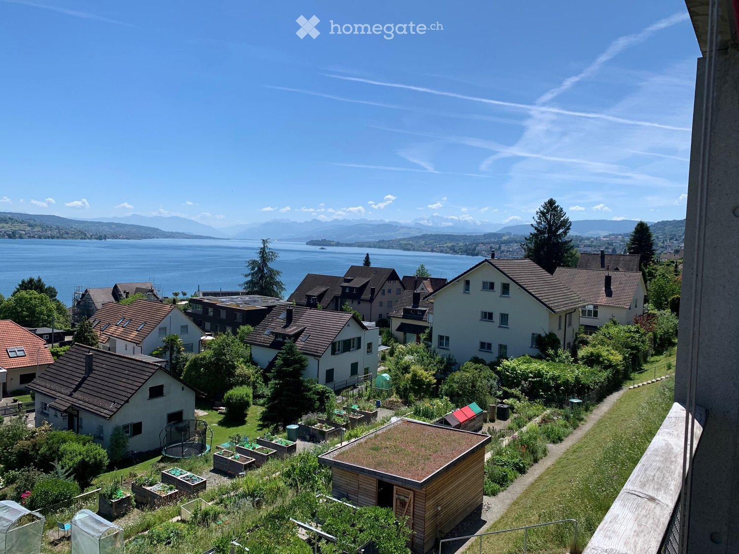 A scenic garden area with raised beds, a trampoline, and a small wooden shed, overlooking a lake and distant mountains.