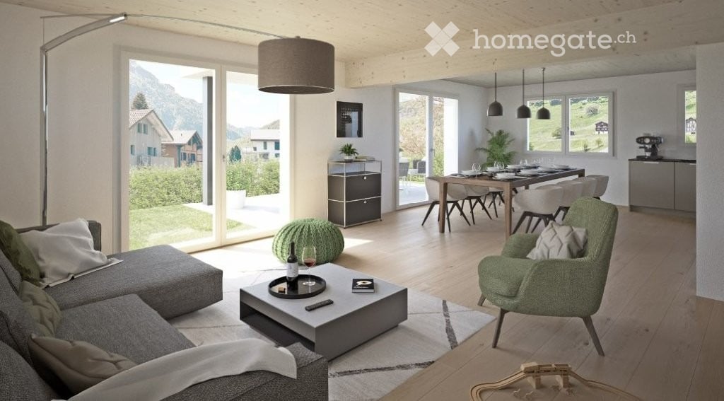 Open-plan living and dining area with large windows offering a scenic mountain view. Features a grey sectional sofa, coffee table, green armchair, dining table with chairs, and modern lighting.
