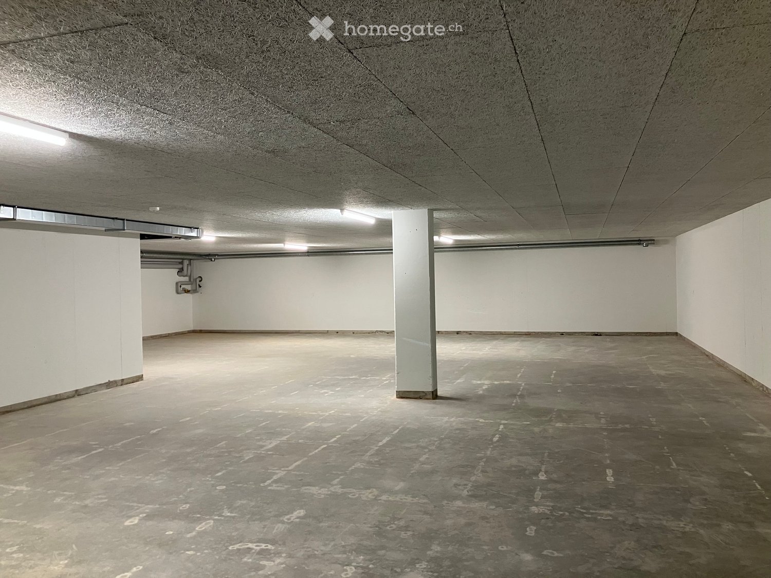 Empty underground parking space with concrete floors, white walls, and fluorescent lighting.