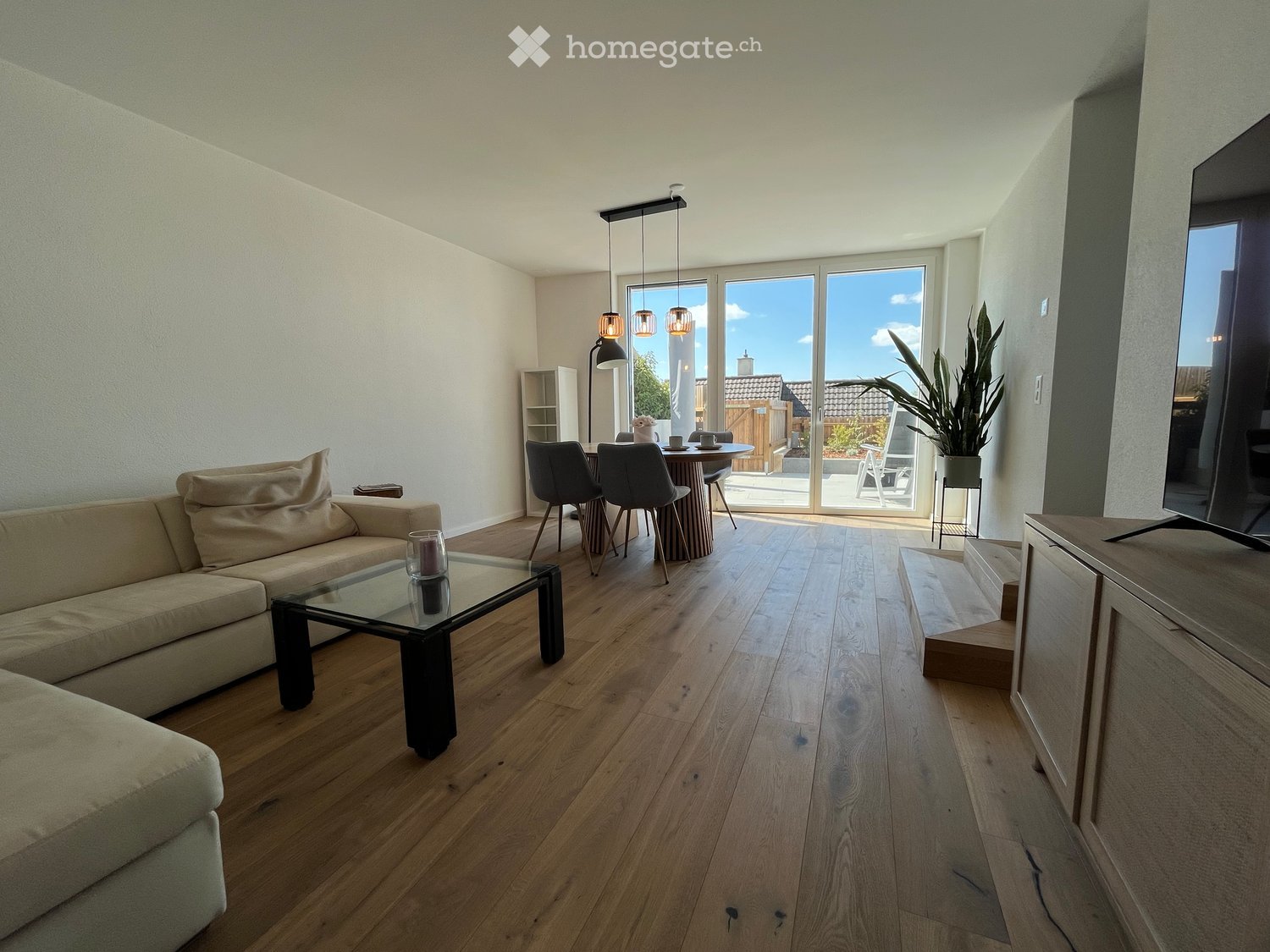living room with dining area, wooden floor, large windows, sliding glass doors to balcony, sofa, coffee table, dining table, chairs, TV, potted plant