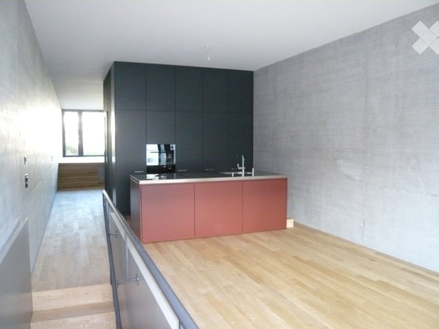 Modern kitchen with a red island, dark cabinets, and a light wooden floor. The space is open and features a staircase leading to another level.