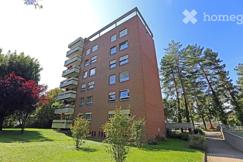 A modern, multi-story brick apartment building with balconies and large windows, surrounded by a well-maintained lawn and trees.