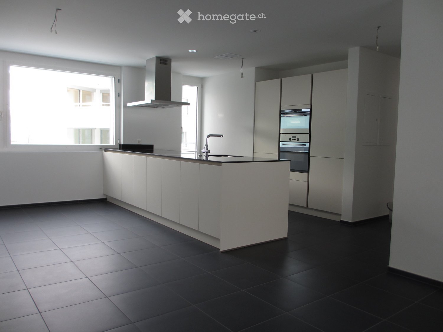Modern kitchen with white cabinets, black tiled floor, central island, sink, faucet, oven, and range hood.