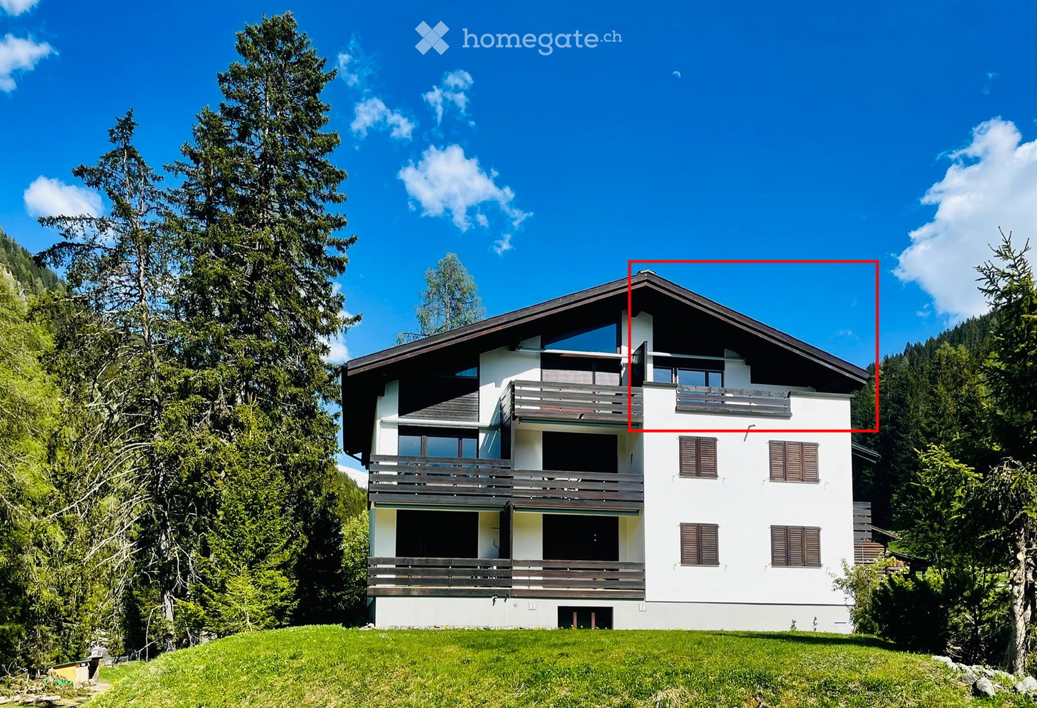 A two-story white house with dark brown shutters and balconies, surrounded by lush green trees and a grassy lawn.