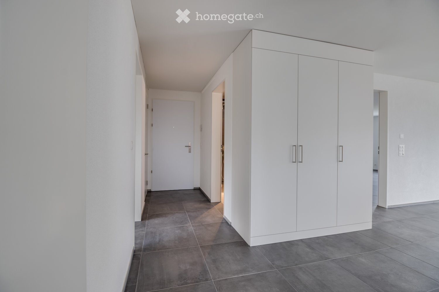 Empty hallway with white walls, dark tiled floor, built-in white cabinetry, and several doors leading to other rooms.