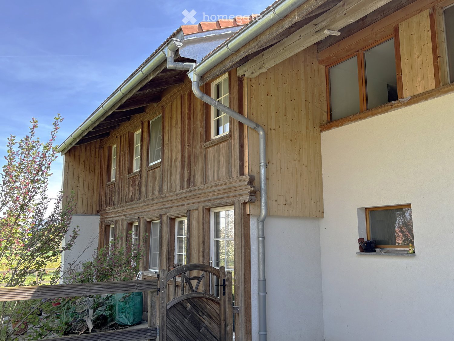 House. Two-story wooden house with a mix of wooden and plaster walls, multiple windows, and a small balcony with a window box on the right side.