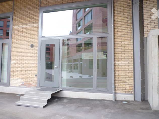 Entrance to a building with a raised ground floor, brick walls, and large glass doors.