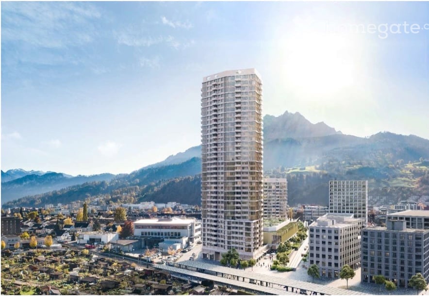 A modern high-rise building surrounded by smaller structures and a scenic mountainous backdrop.