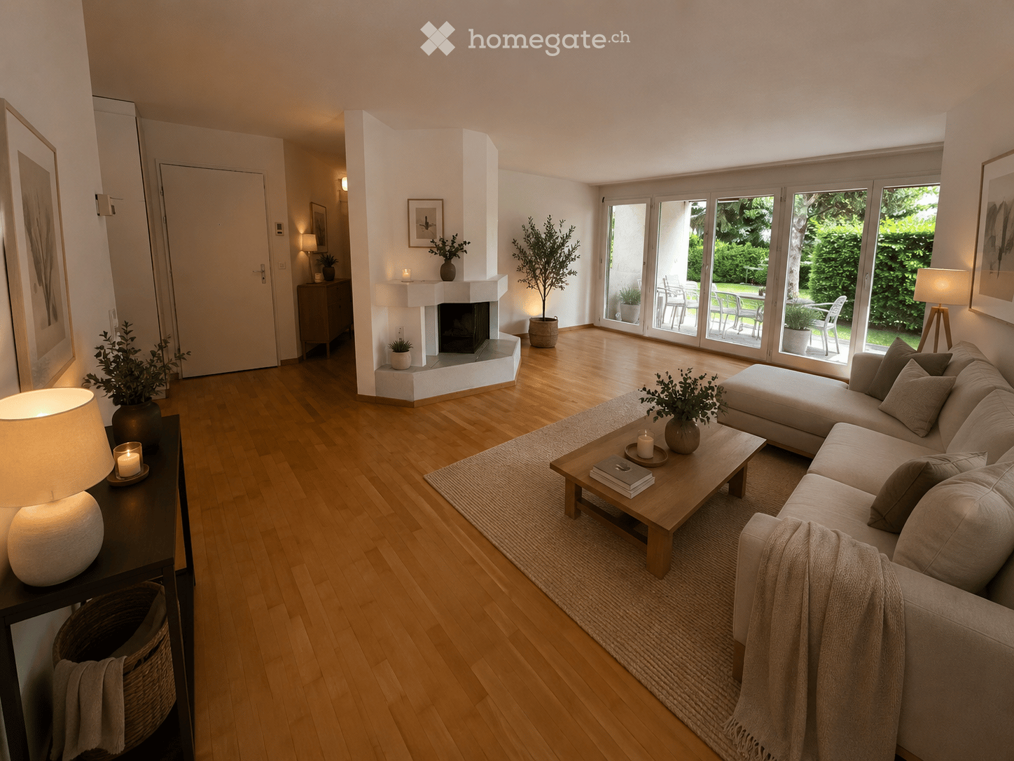 Bright living room with wooden flooring, large windows, a fireplace, a sectional sofa, coffee table, side table, and decorative plants.