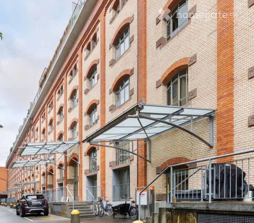 Modern multi-story building with brick facade, large arched windows, and covered entrance area with glass canopy.
