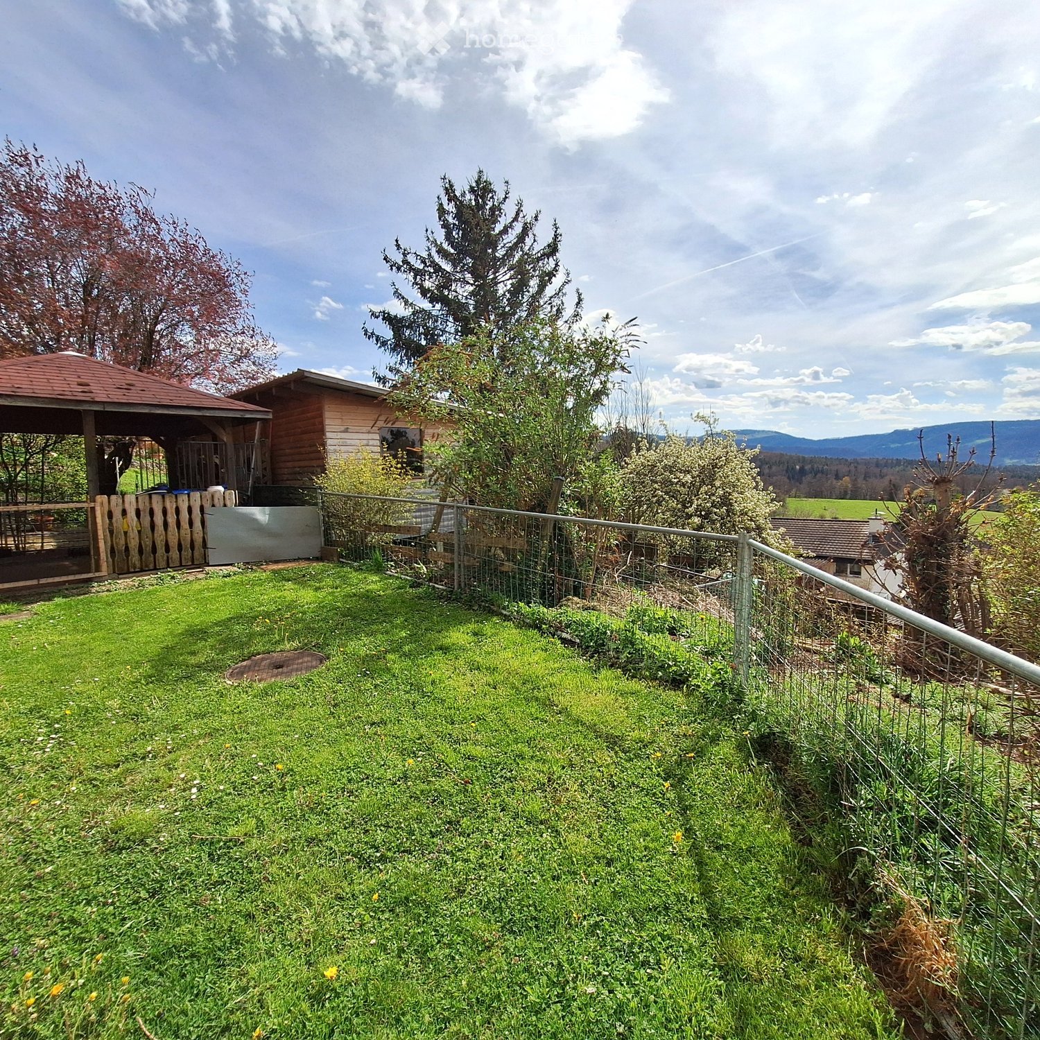 Green lawn, wooden fence, trees, mountains in the background