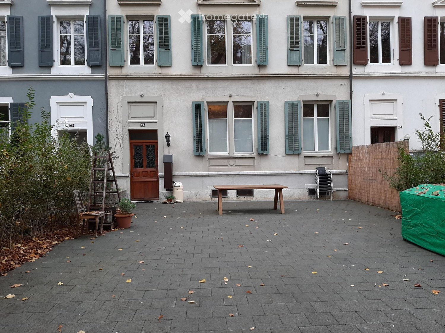 Brick paved courtyard with a wooden table, plants, trash bin, and a ladder