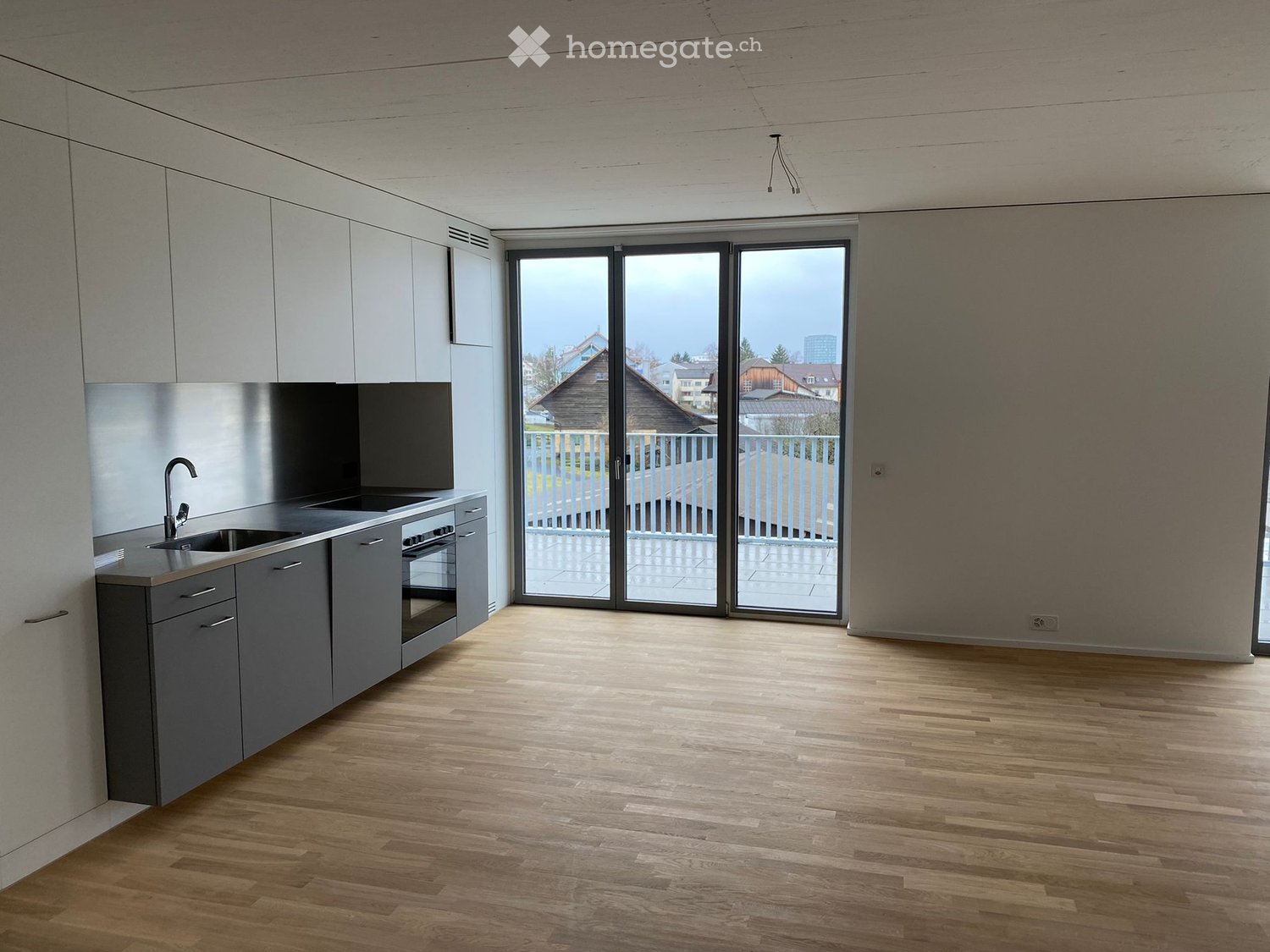 Modern kitchen with grey cabinets, wooden flooring, and large sliding glass doors leading to a balcony.