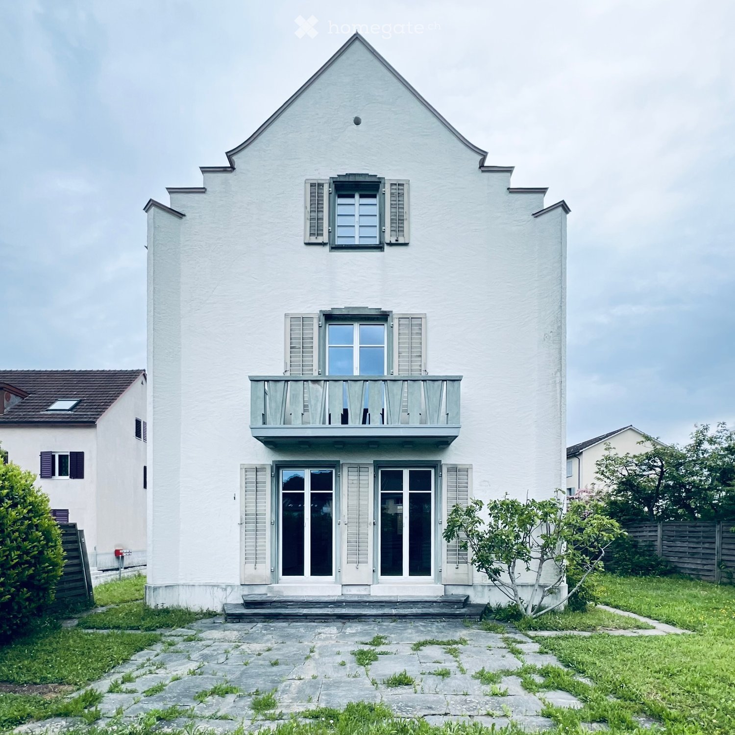 Two-story white house with a balcony, large windows, and a stone pathway leading to the entrance.