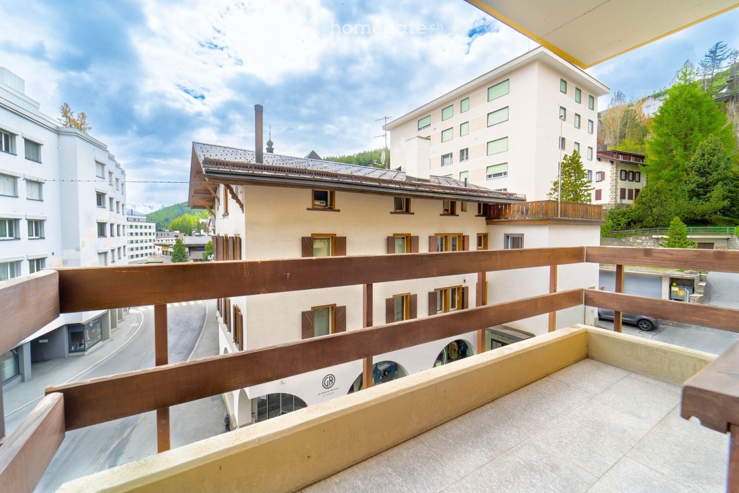 Balcony overlooking a town with multi-story buildings, wooden railings, and a clear sky.