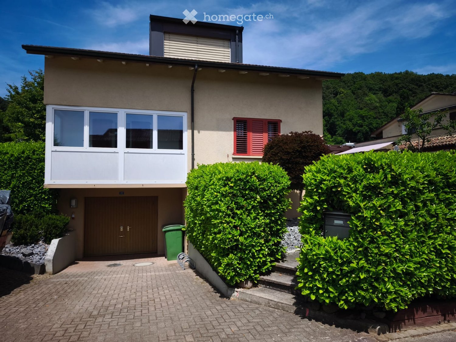 Two-story house with beige facade, large windows, red shutters, and a raised ground floor entrance.