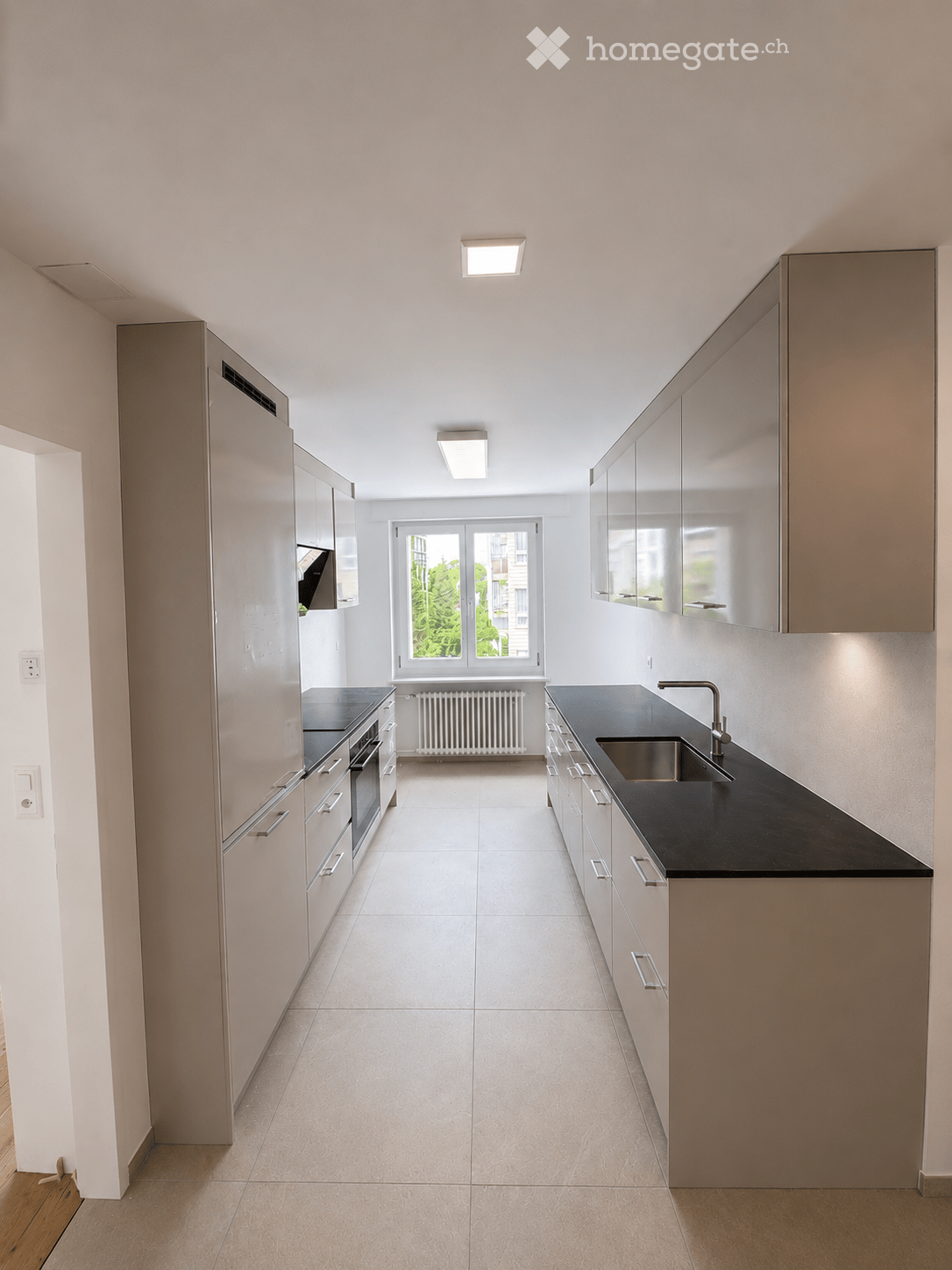 Modern kitchen with white cabinets, black countertops, and a stainless steel sink. Features include built-in oven, ample storage, and a large window with a view of greenery.