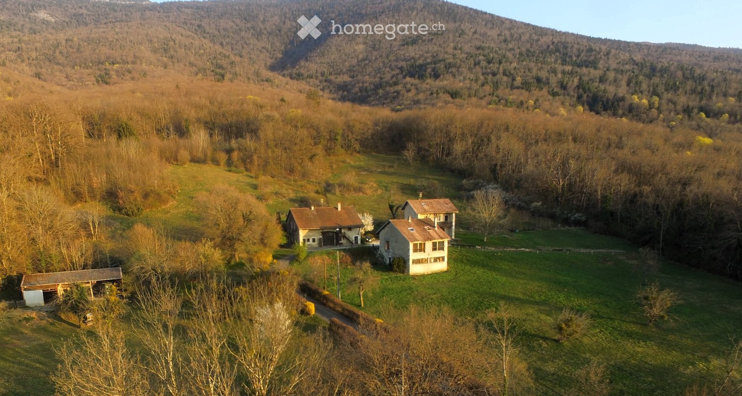 Aerial view of a rural property with three houses, surrounded by forested hills and open fields.