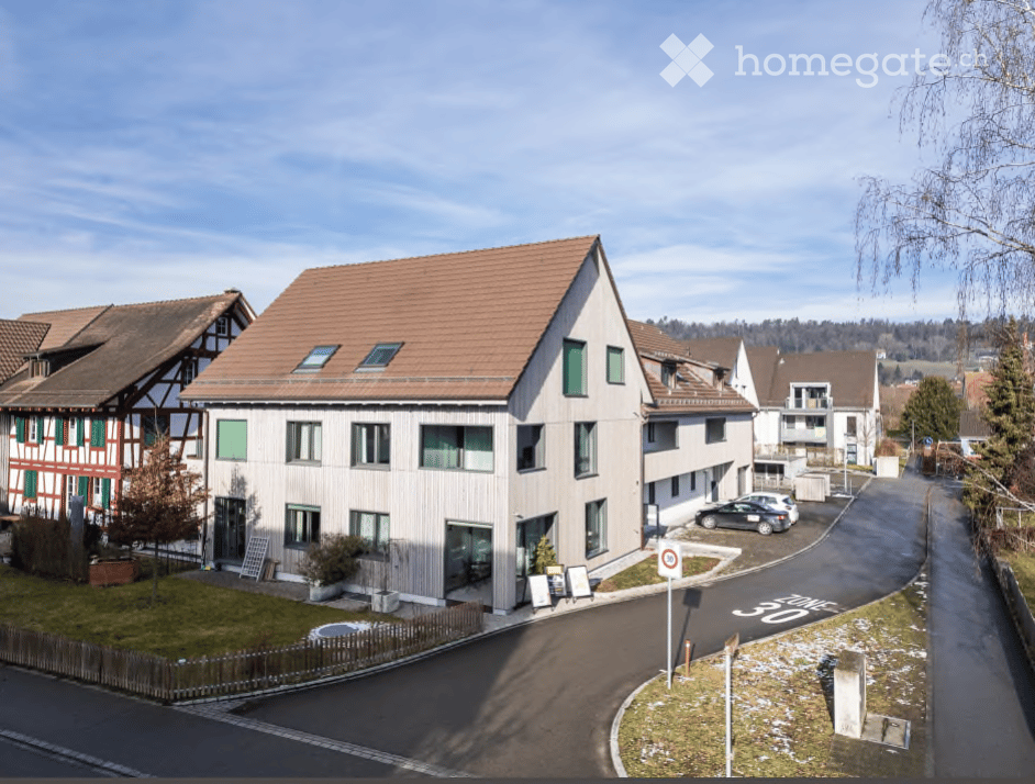 Modern two-story residential building with a brown tiled roof, multiple windows, and a small garden area in front.