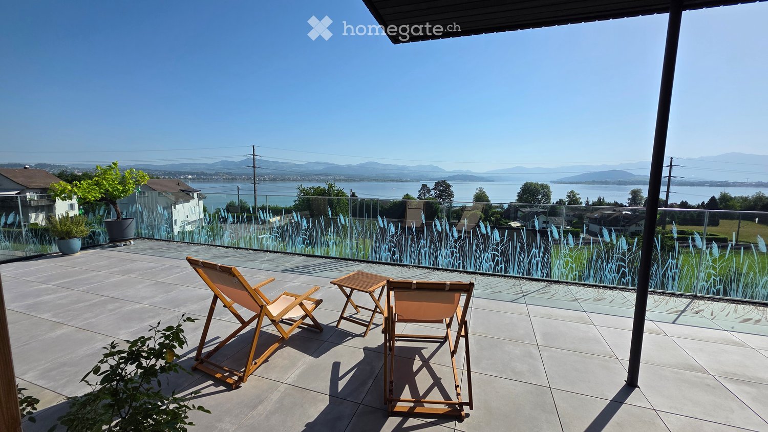 Balcony with a scenic view of a lake and mountains, featuring two wooden chairs and a small table.