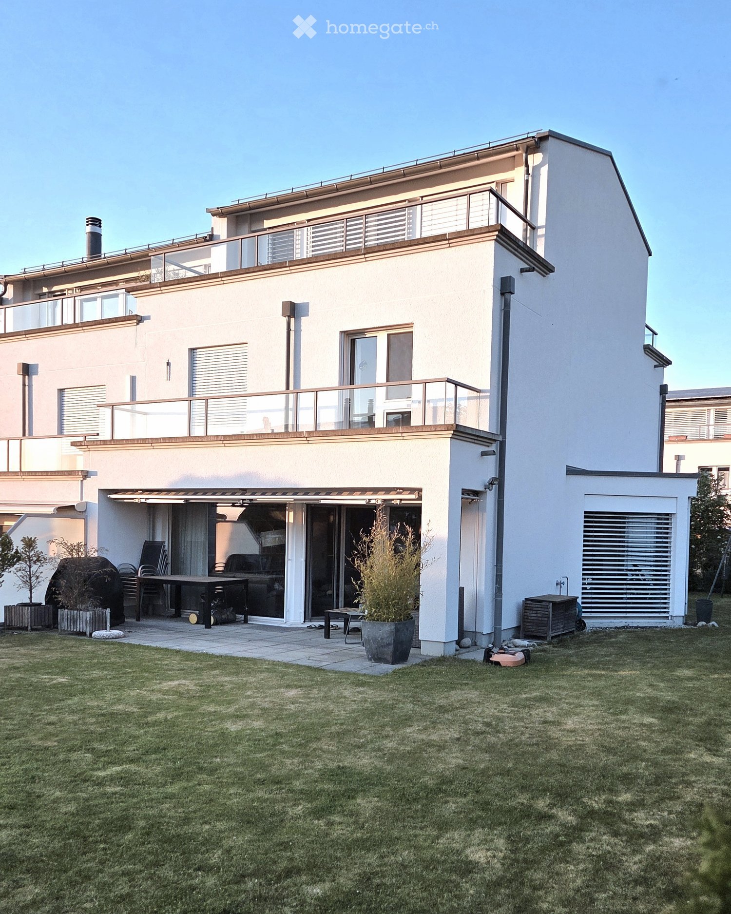 House. Modern two-story house with white exterior, large windows, balconies, and a well-maintained lawn.