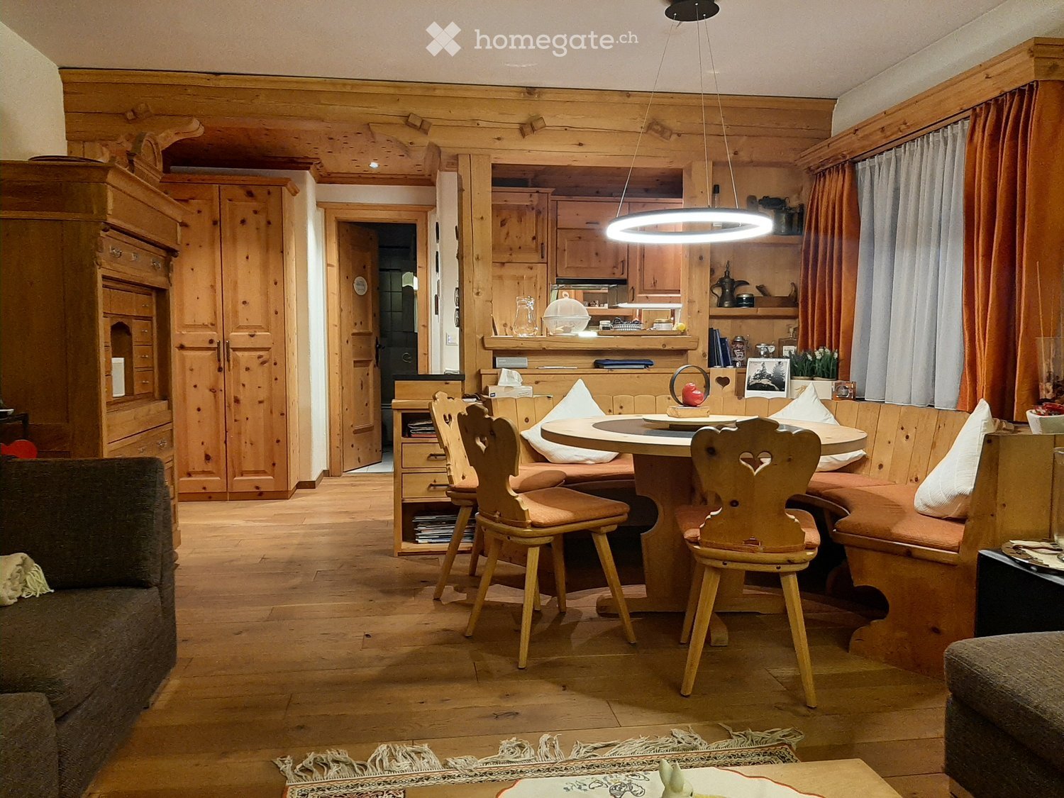 Cozy, wooden-furnished living and dining area with a sofa, dining table, chairs, kitchen area, and wooden cabinetry.
