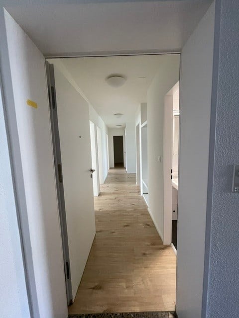 Empty hallway with white walls, wooden flooring, and several closed doors on both sides.