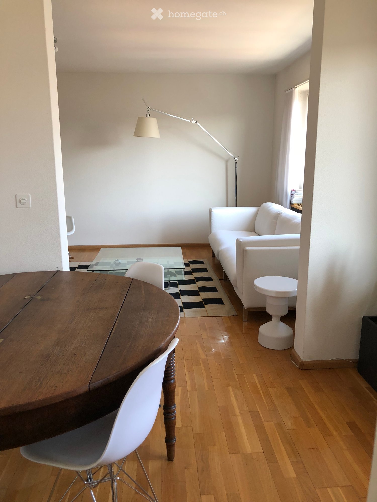 Modern living room with white sofa, wooden table, white chairs, floor lamp, and a small white stool.