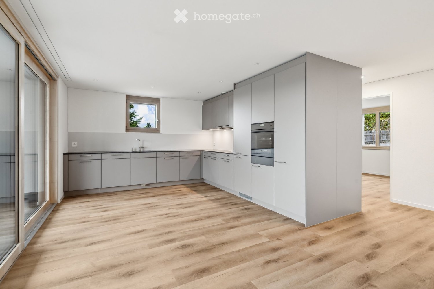 Modern kitchen with light grey cabinets, wooden floors, central island with a sink, under cabinet oven, and extractor hood