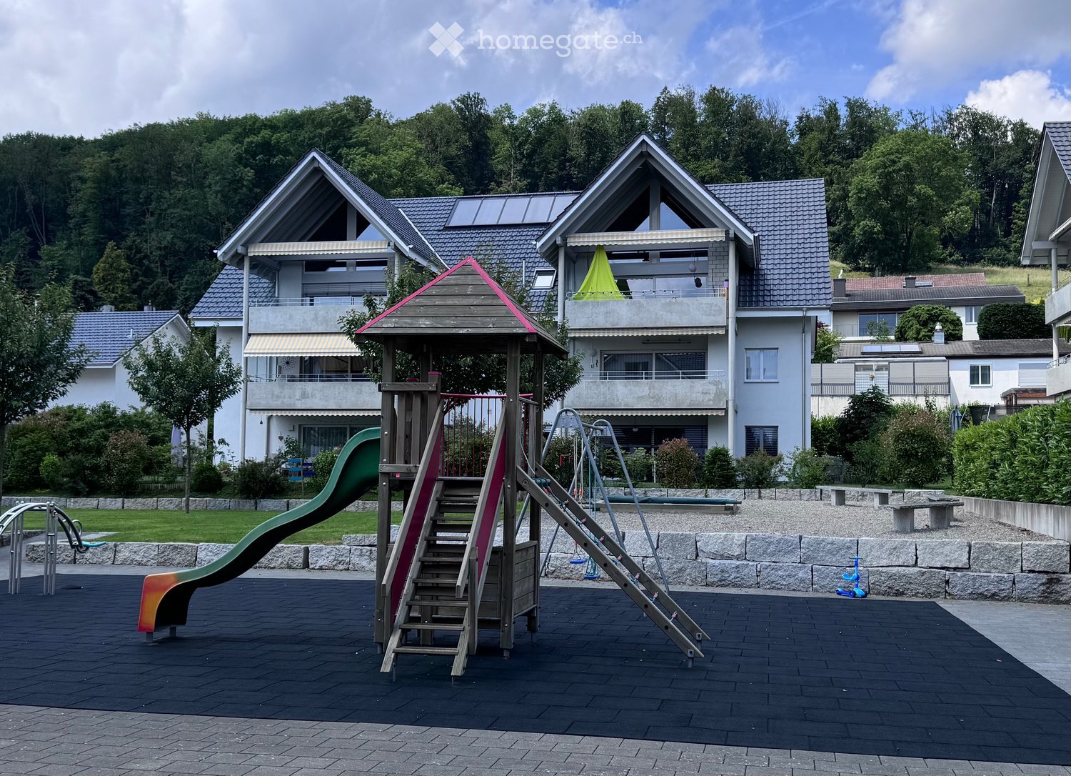 Outdoor playground with a slide, climbing frame, swing, and benches.