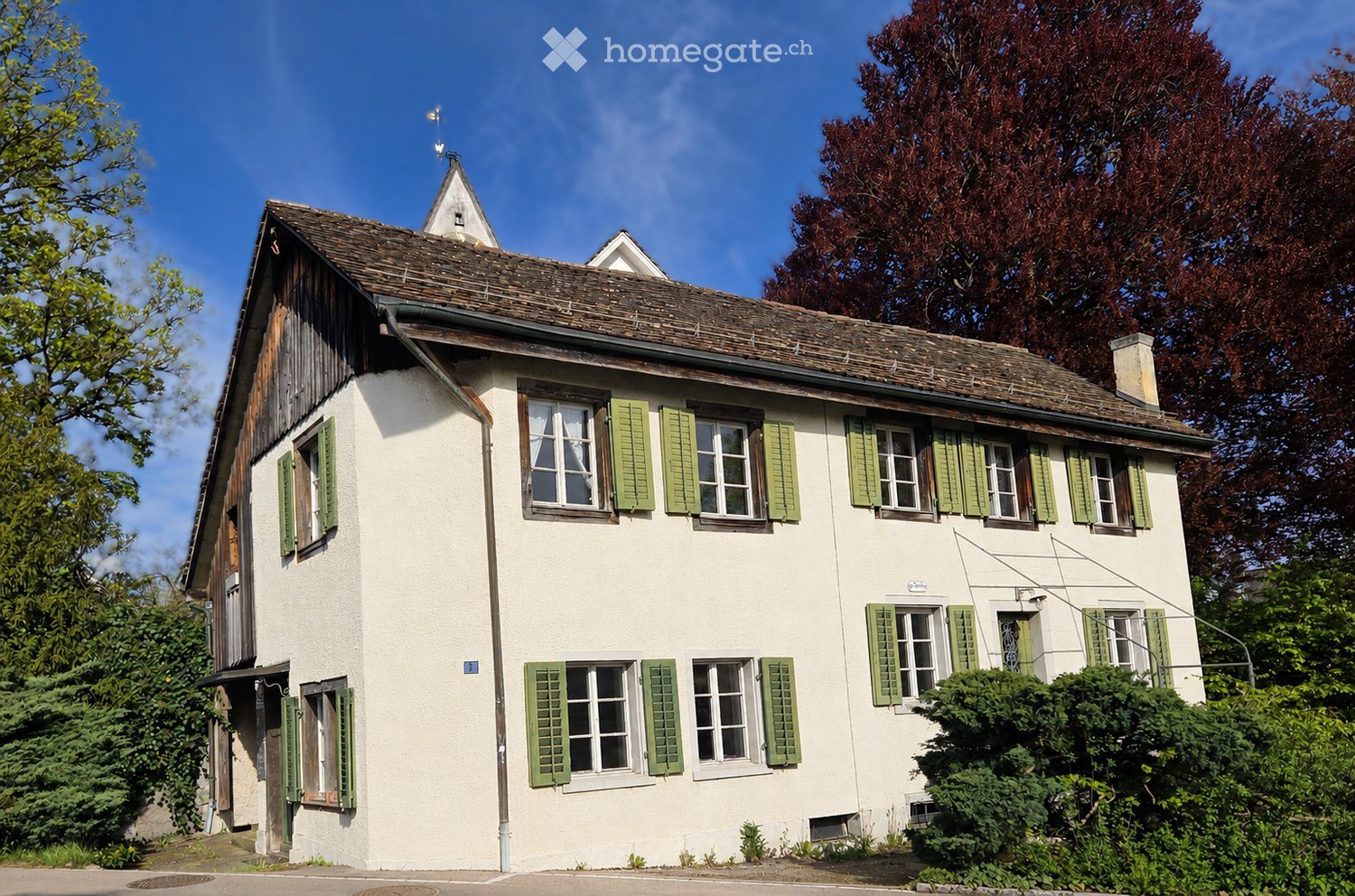 Two-story white house with green shutters, multiple windows, and a pitched roof.