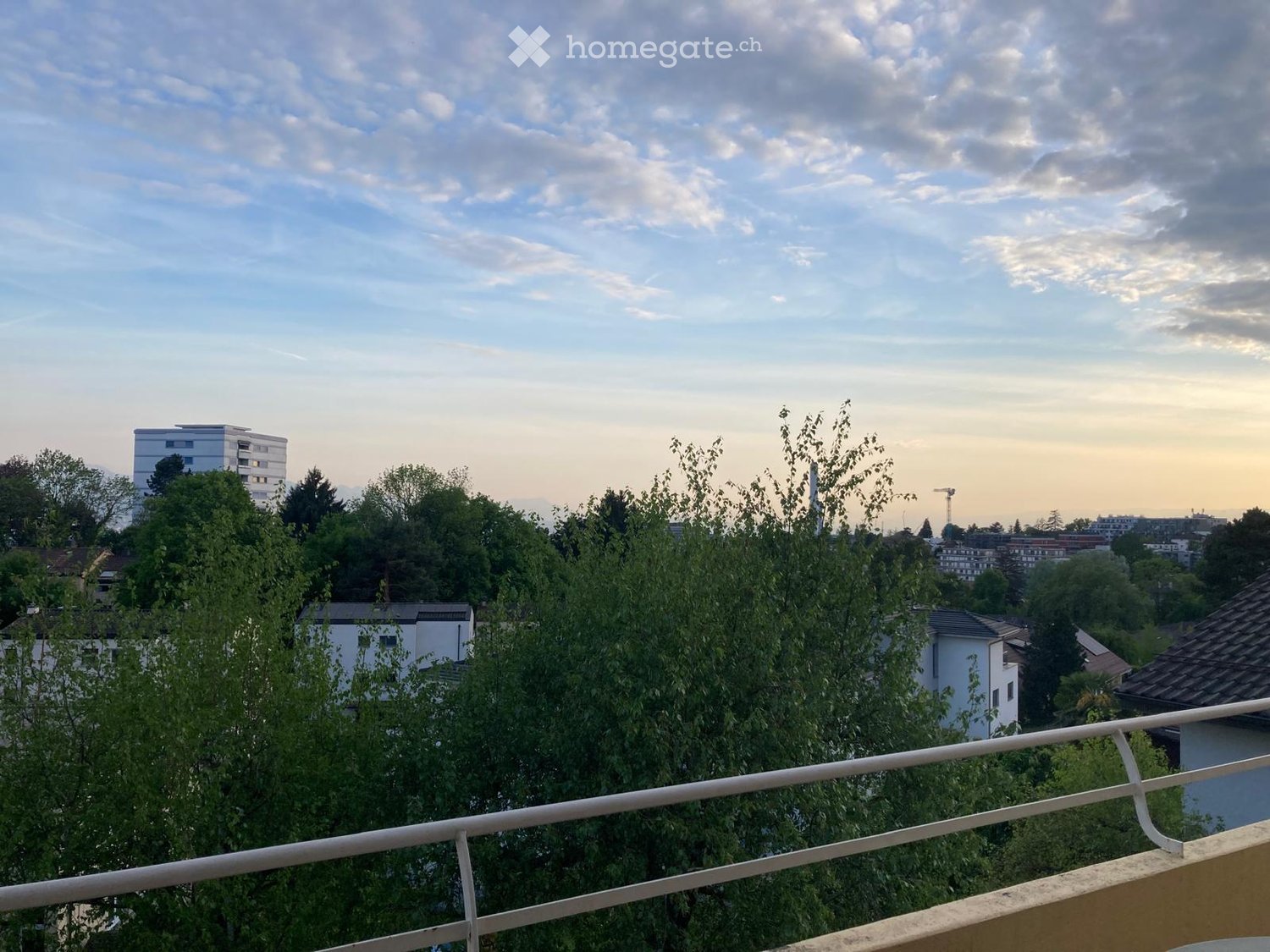 Balcony / Terrace. Balcony overlooking a cityscape with trees, buildings, and a partly cloudy sky.
