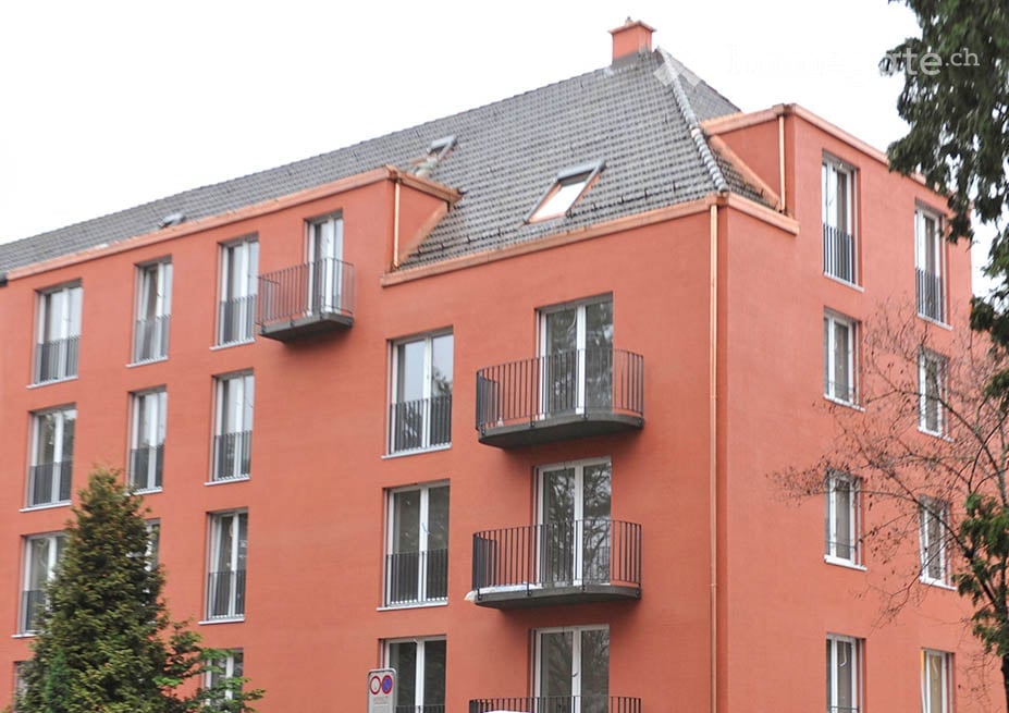 Four-story apartment building with orange-red facade, multiple windows, and several balconies.