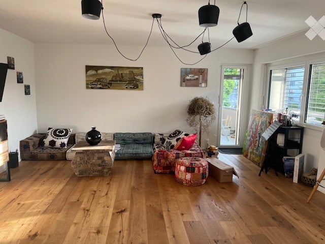 Living room with wooden flooring, a sofa, coffee table, ottoman, and decorative items including a vase and picture frames.